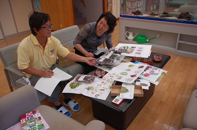 アーティスト・野田三千代さんの海藻おしばの作品を並べて打ち合わせ中の白井さんと池森さん