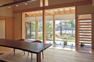 キッチンからサンルーム越しに庭を見る。リビングの床はアカマツ。ダ イニングテーブルは四国から取り寄せたウォールナットの一枚板を加工 したもの。